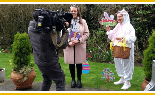 Easter interview: woman in pink coat, bunny costume person with basket, cameraperson filming.